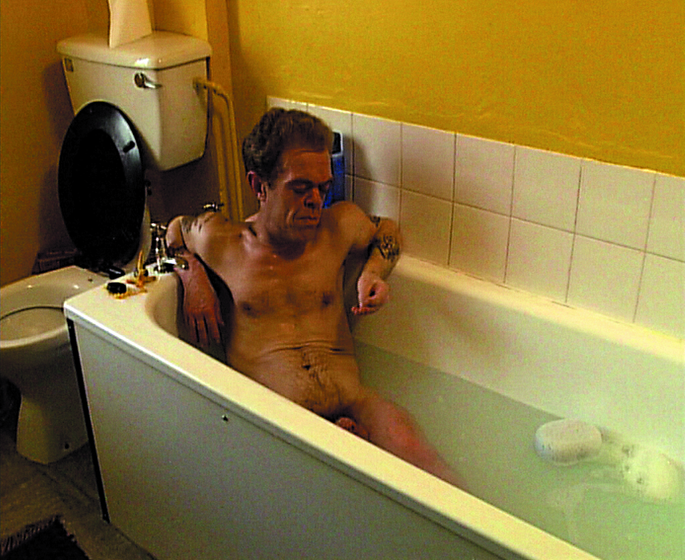 This still shows a runtish man naked in a filled bathtub. He looks lost in thought at his right hand.