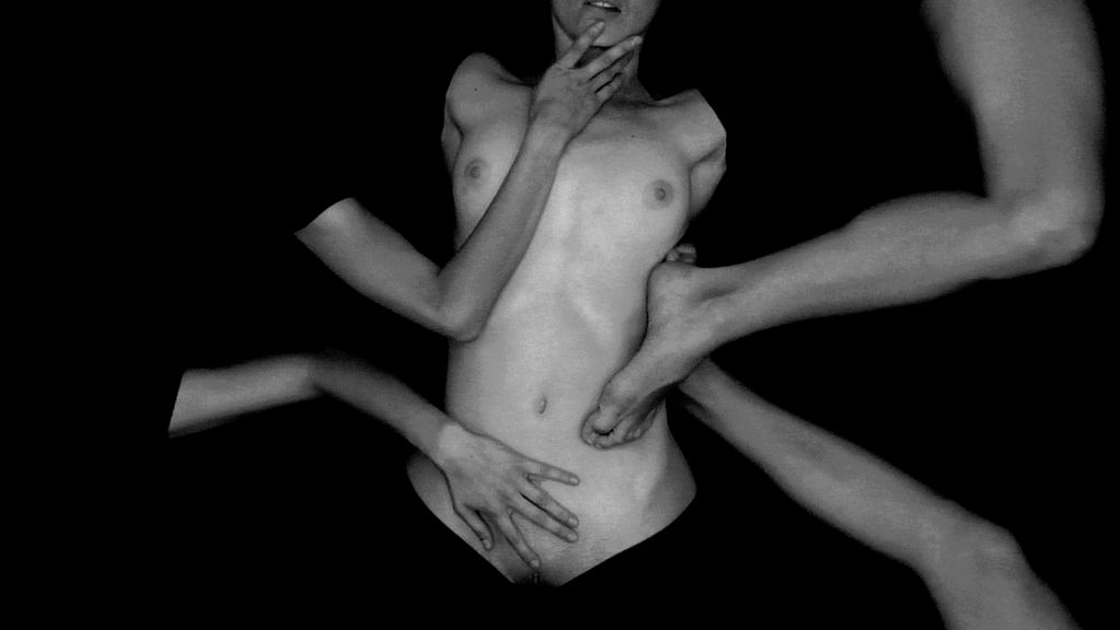 In diesem Video Still ist ein weiblicher, scheinbar abgeschnittener Torso zu erkennen, der von zwei Händen und zwei Füßen berührt wird. Agneta Grzeszykowska, Sammlung Goetz München