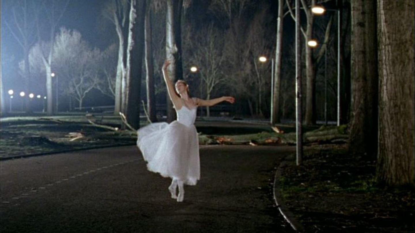 Video Still, das eine Balletttänzerin beim Spitzentanz in weißem Kostüm auf einem Weg in einem beleuchteten Park bei Nacht zeigt. Guido van der Werve, Sammlung Goetz München 