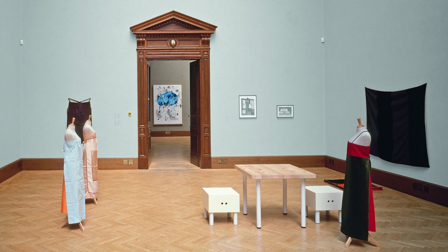 Hier ist ein Ausstellungsraum mit Textilarbeiten, Möbeln und Skizzen von Andrea Zittel zu sehen.