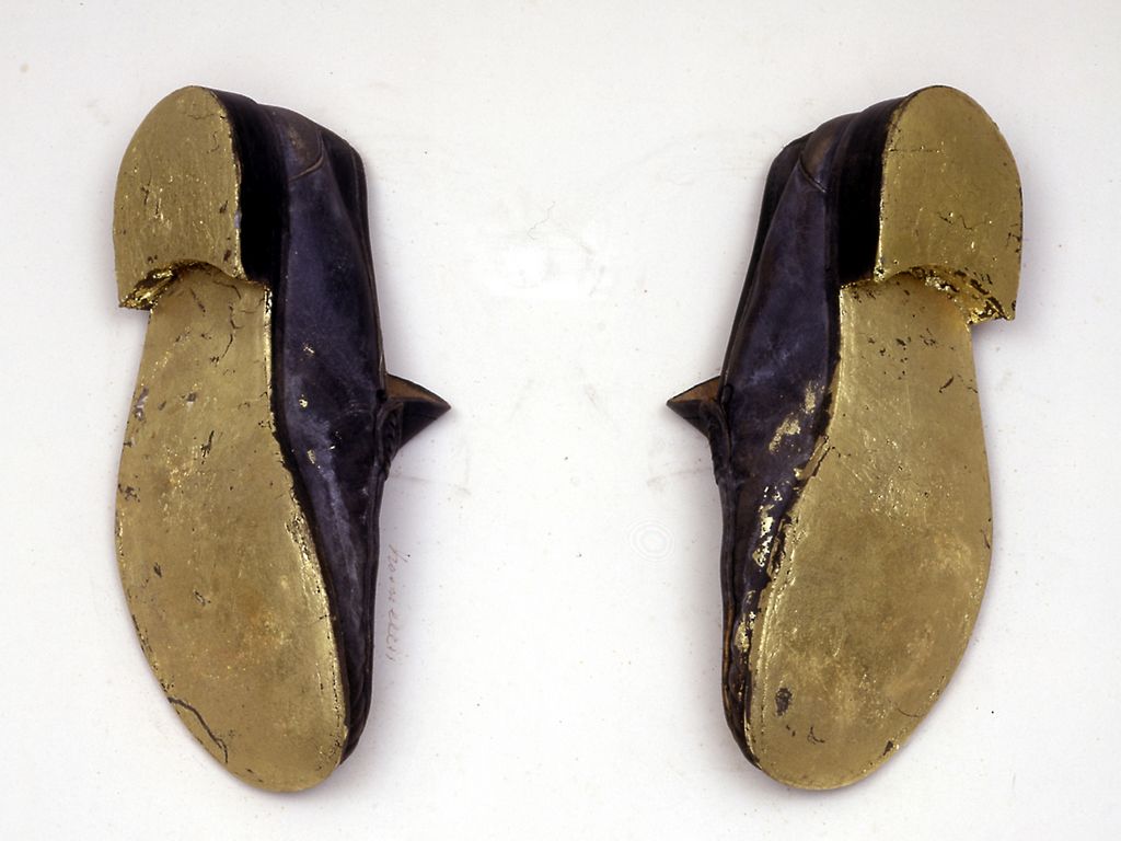 A pair of black leather slippers with gold leaf covered soles that seem to be hung on the wall.
