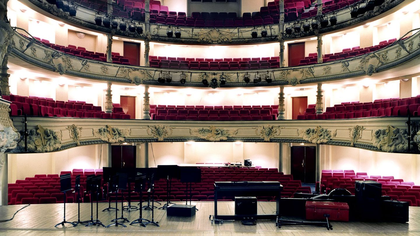 Auf dieser Fotografie ist ein leerer, barocker Konzertsaal beziehungsweise Opernsaal von der Bühne aus zu sehen. Auf der Bühne stehen Notenständer, ein elektrisches Klavier und sonstiges musikalisches Equipment. Candida Höfer, Sammlung Goetz München