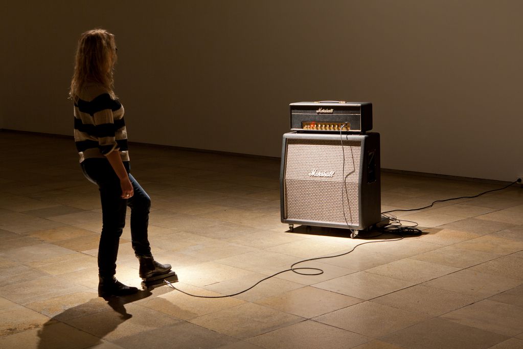 This photograph shows a woman in a room with a Marshall amplifier. She is stepping on a pedal connected to the amplifier and thus appears to be able to operate it. Janet Cardiff/George Bures Miller, Sammlung Goetz Munich