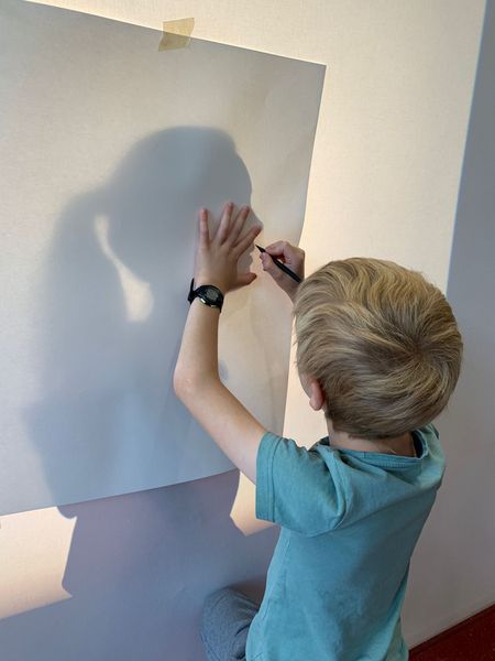 Kind zeichnet Schattenriss einer Person mit Pferdeschwanz-Frisur nach
