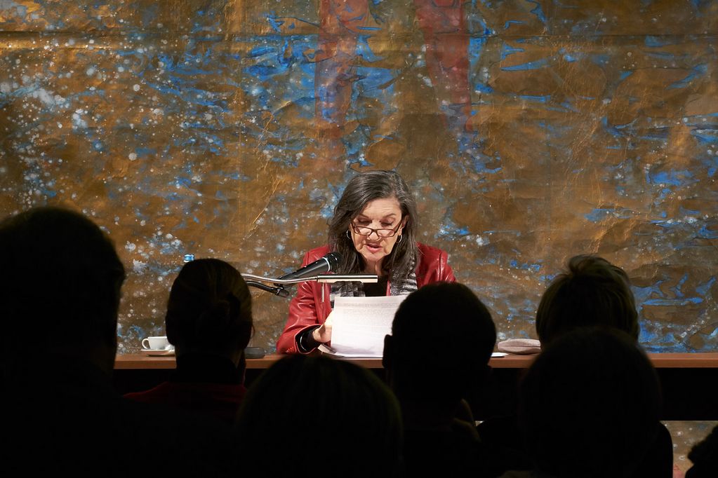 A woman with dark hair can be seen reading in front of a large-format painting by Michael Buthe. In front of her is a row of shadowy, dark heads of the audience. Sammlung Goetz Munich