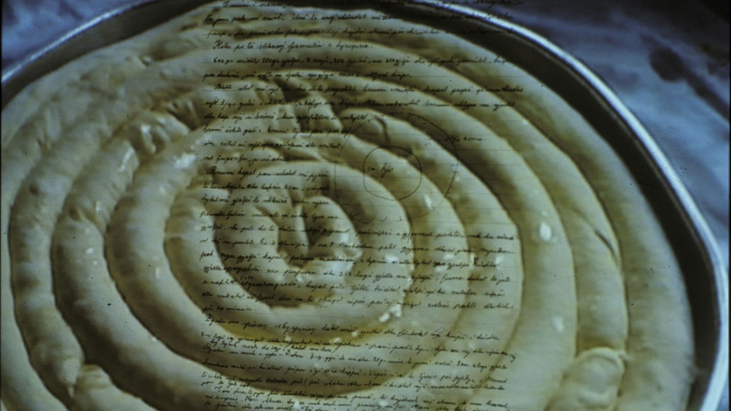 This recording is a film still by the artist Anri Sala. It shows an Albanian byrek in a baking tin, which is overlaid with the image of a handwritten letter.