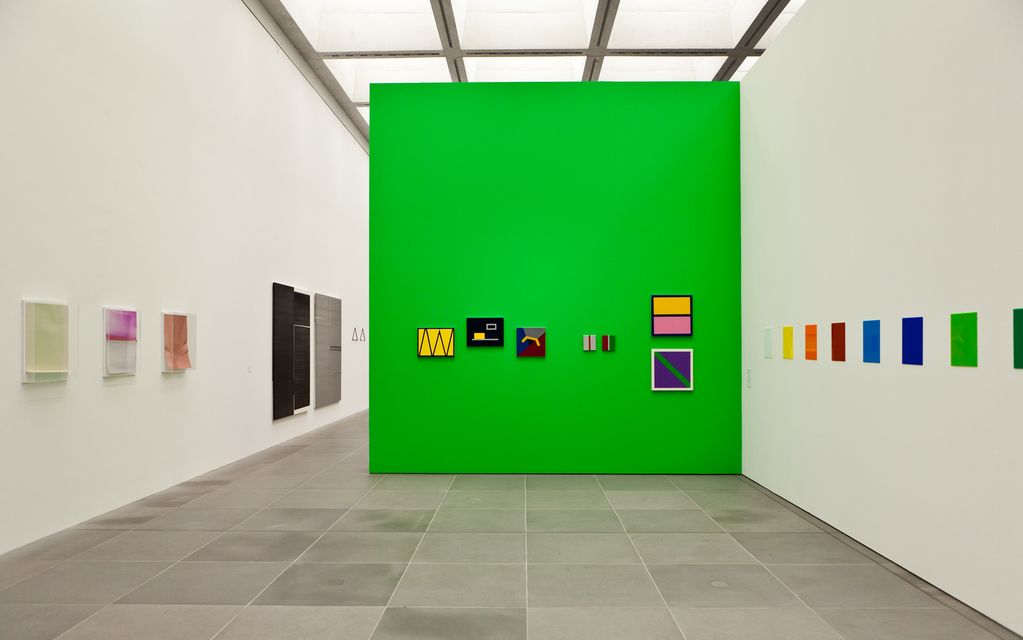 Exhibition view showing a drawn-in bright green wall in the midst of white walls. On it are colourful two-dimensional works by the artist Gerwald Rockenschaub. On the wall to the right of this are also monochrome, differently coloured and small-format plastic panels by the same artist. On the wall to the left are photographic works in plastic display cases by the artist Wolfgang Tillmans. Wade Guyton/Gerwald Rockenschaub/Wolfgang Tillmans, Sammlung Goetz Munich