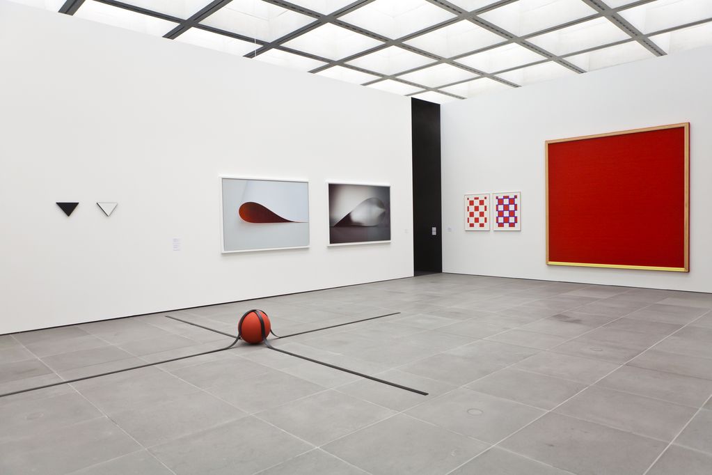 Installation view of various minimalist works by different artists. All works are in the colours red, white and/or black and are located in a white room. Blinky Palermo/Reiner Ruthenbeck/Wolfgang Tillmans/Rosemarie Trockel, Sammlung Goetz Munich