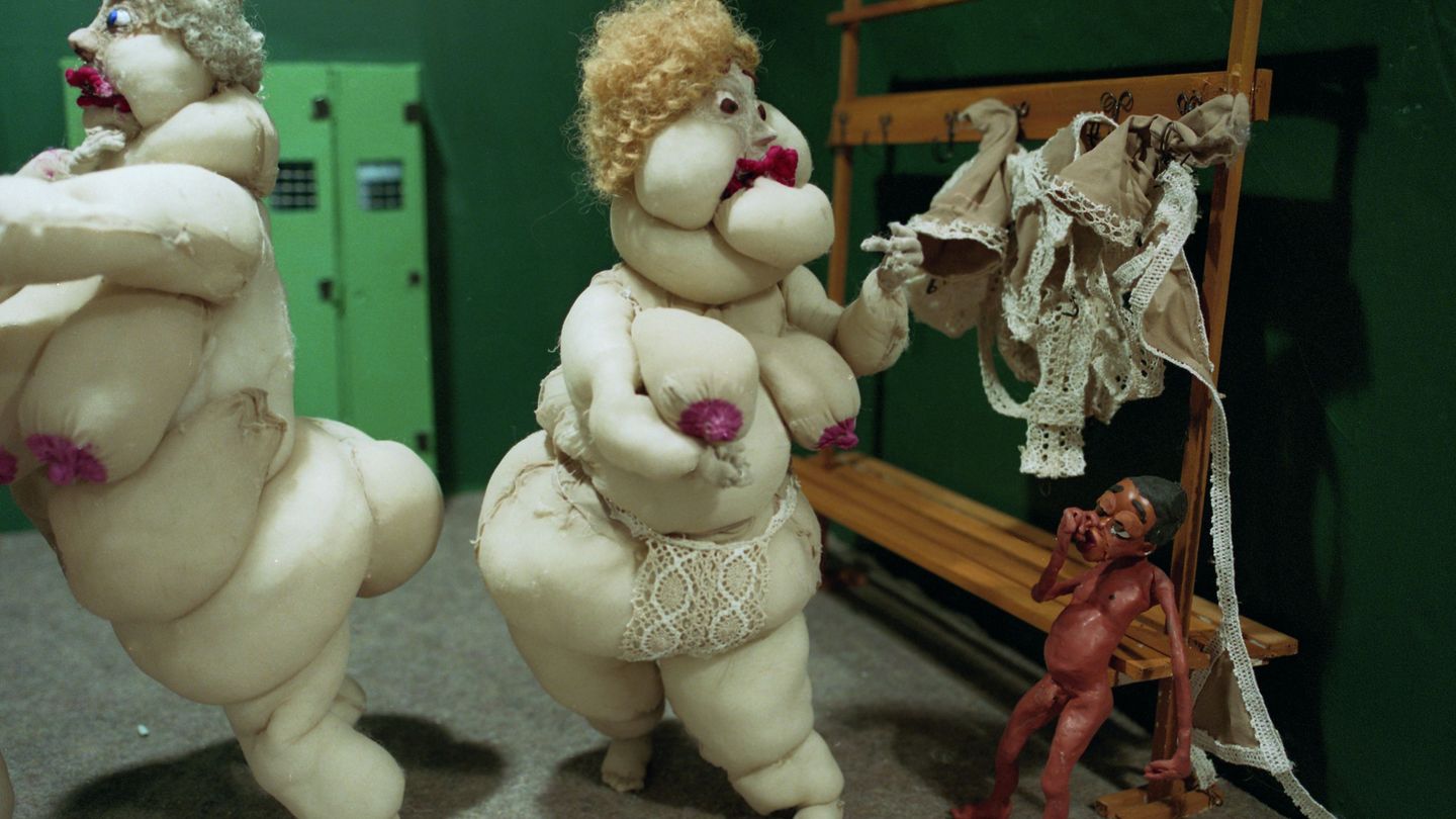 The video Still shows two very fat, naked and white female dolls made of fabric in a changing room together with a small black boy made of plasticine. Nathalie Djurberg & Hans Berg, Sammlung Goetz Munich