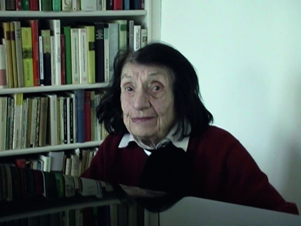 Video Still einer älteren Dame am Klavier, hinter ihr ein volles Bücherregal. Frank Stürmer, Sammlung Goetz München