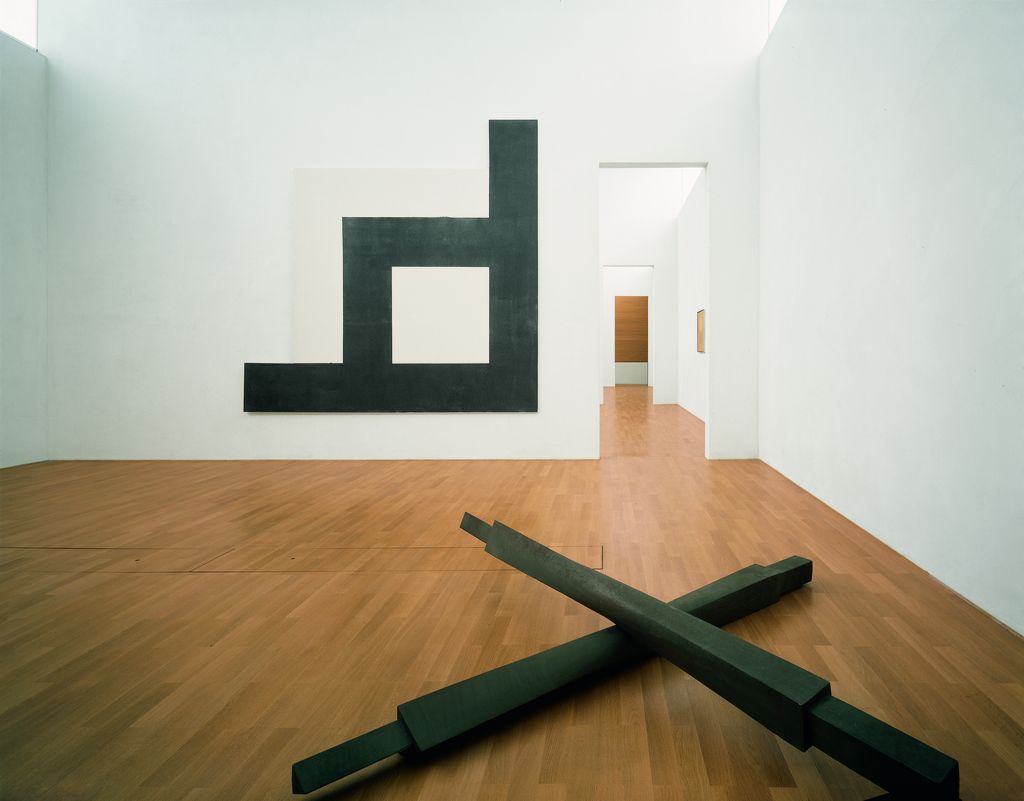 Diese Fotografie zeigt eine Installationsansicht in den Räumlichkeiten des Ausstellungsgebäudes mit schwarzen, minimalistischen Arbeiten von Bruce Nauman und Michael Heizer.