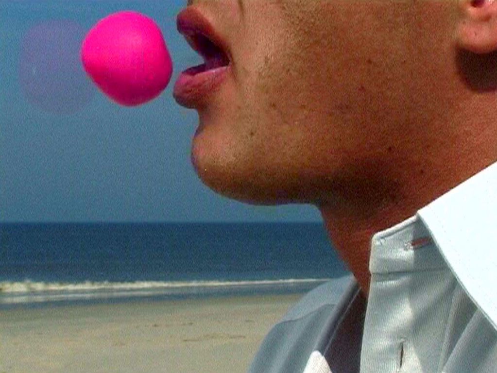 Pink ball in front of a male, open mouth, a beach scene in the background. Annika Larsson, Sammlung Goetz Munich