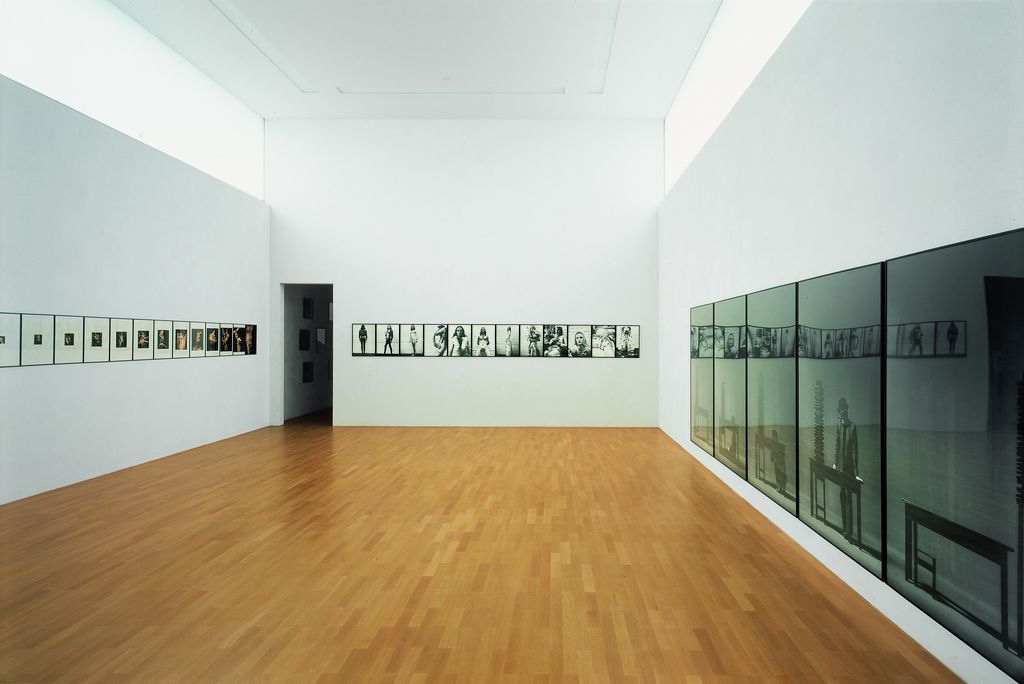 Dies ist eine Installationsaufnahme. Sie zeigt auf der Wand geradeaus kleinere Schwarzweißfotografien des Künstlers Jürgen Klauke. An der Wand rechts sind großformatige Schwarz-Weiß-Arbeiten des Künstlers zu sehen, während links kleinformatige Farbfotografien hängen. Alle Arbeiten sind jedoch auf den jeweiligen Wänden Rahmen an Rahmen gehängt.