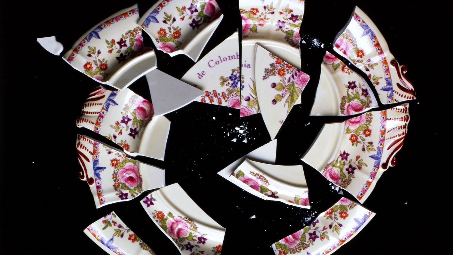 Video Still showing a cracked plate on a black background, originally adorned with a floral border and the saying "Republica de Colombia para siempre". Juan Manuel Echavarria, Sammlung Goetz Munich