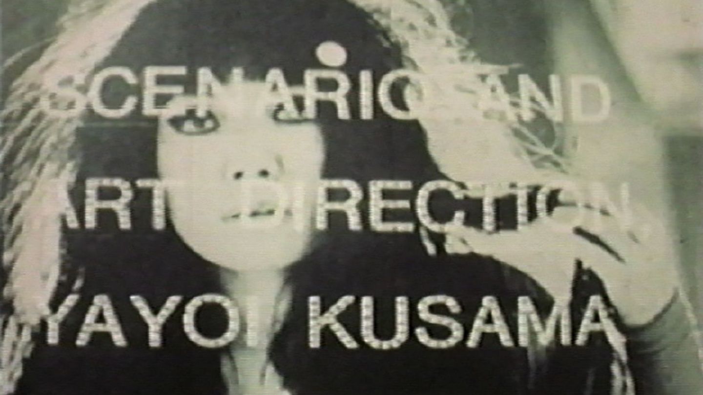 This screenshot shows the artist at a young age. The picture is in black and white, but you can see that her eyes are heavily and darkly made up. Above her face is written in white letters: "Scenario and art direction Yayoi Kusama".