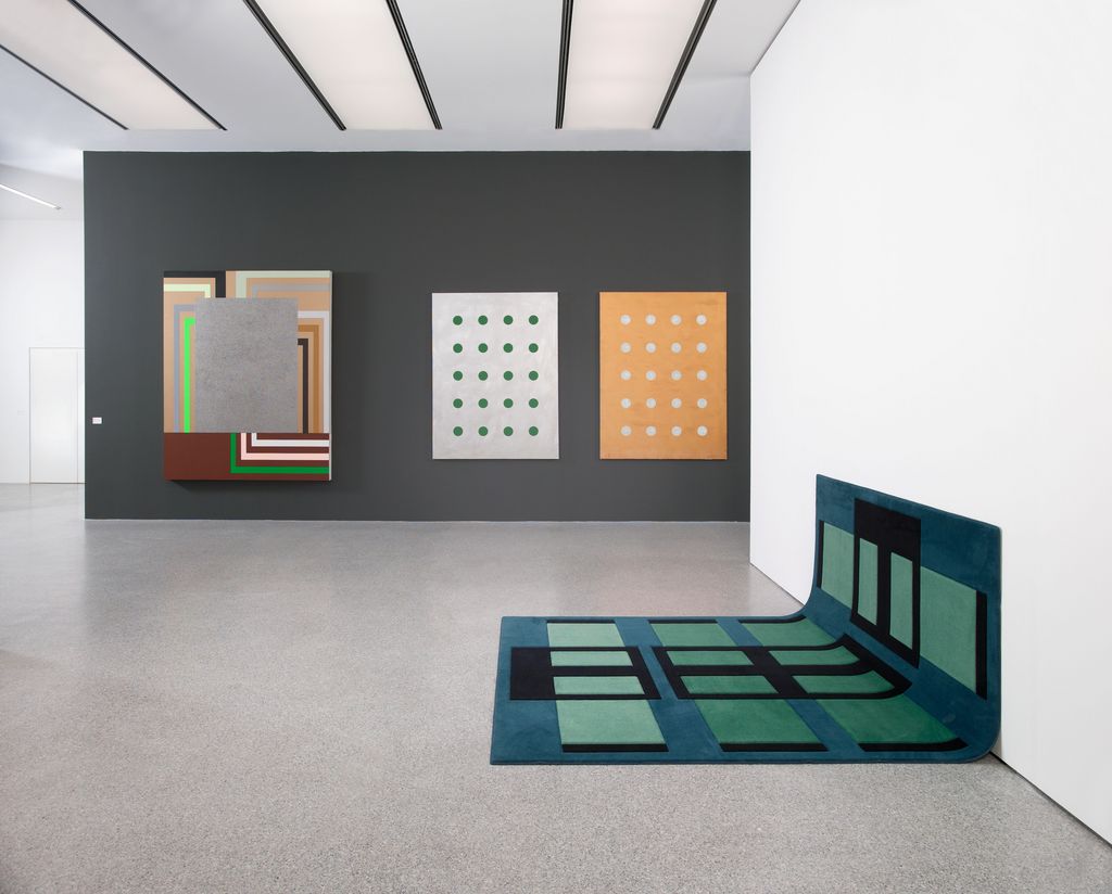 Exhibition view with multi-coloured, minimalist works by the artists Peter Halley, John Armleder and Andrea Zittel. These are three two-dimensional paintings and a carpet that functions as both a wall and floor rug. Sammlung Goetz Munich