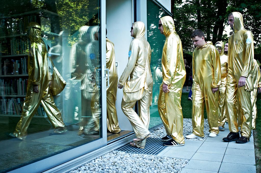 Performance Still einer Gruppe von Menschen, allesamt in goldene Lurex-Einteiler gekleidet, die im Begriff sind den Eingangsbereich der Sammlung Goetz nacheinander zu betreten. Paweł Althamer, Sammlung Goetz München