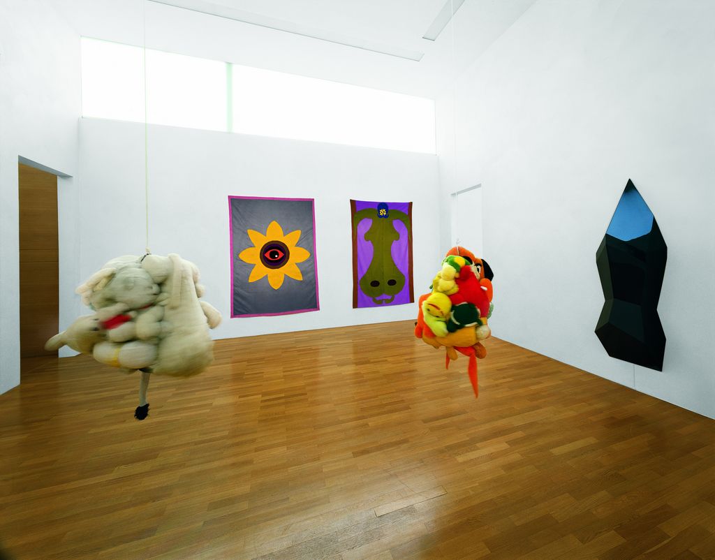 Exhibition view of two tapestries, one wall object, and two objects hanging from the ceiling by American artist Mike Kelley. Mike Kelley, Sammlung Goetz Munich