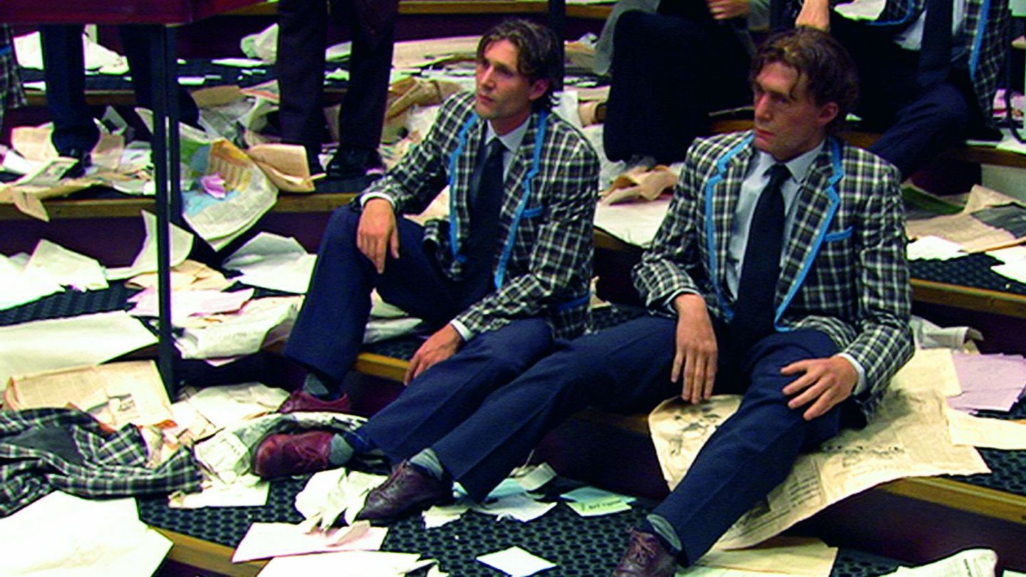 This shot shows a film still of three men dressed alike, with the same hairstyles, sitting exhausted and resigned on broad steps. The floor is full of scattered papers, the contents of which are not discernible. Aernout Mik, Sammlung Goetz Munich