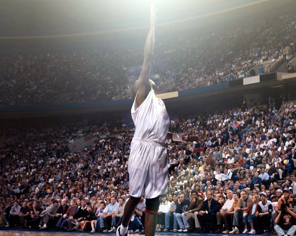 Photography showing a black basketball player stretching his right arm in the air and seeming to reach for a light. A crowded game stadium can be seen in the background. Paul Pfeiffer, Sammlung Goetz Munich