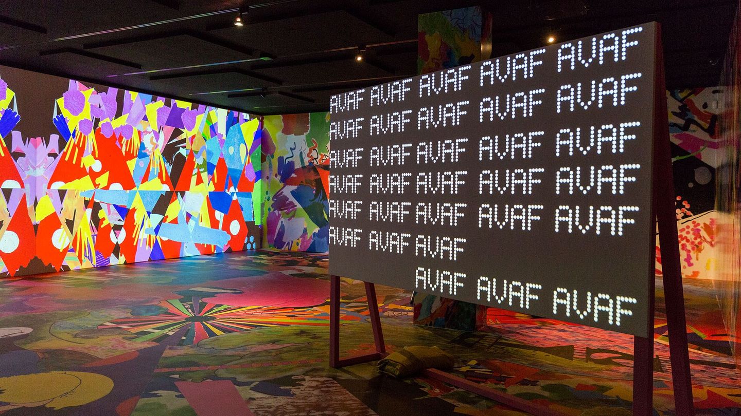 Colourfully decorated room with a board in it on which the acronym AVAF (assume vivid astro focus) is repeated in LED lettering. Sammlung Goetz Munich