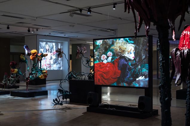 Düstere begehbare Installation mit überdimensionalen Blumenskulpturen und Videoprojektionen