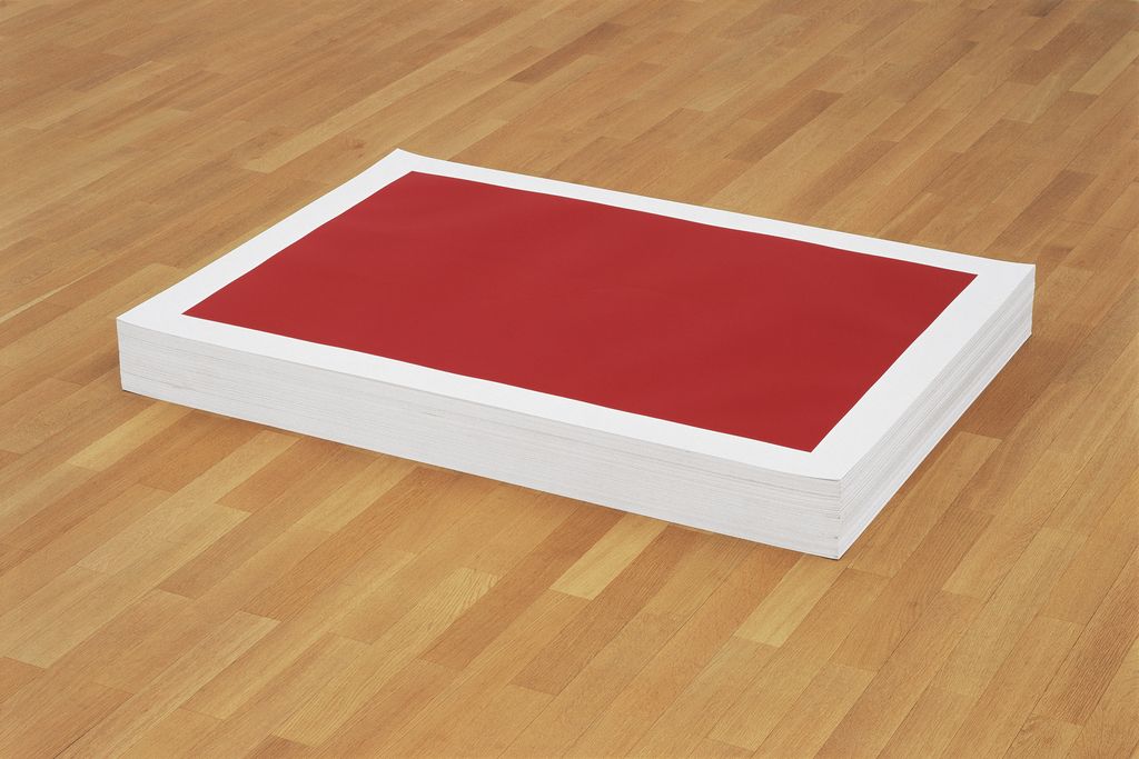Dieses Bild zeigt eine Aufnahme eines Papierstapels mit den Maßen 91 x 125 cm und einer Höhe von 14 cm auf einem hellen Holzboden liegend. Auf dem Papier ist ein großes, rotes Rechteck mit einem weißen Rand in der Form des Papiers gedruckt.