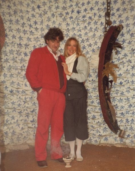 Michael Buthe and Ingvild Goetz standing arm in arm in front of a white wall painted with blue stars. Sammlung Goetz Munich