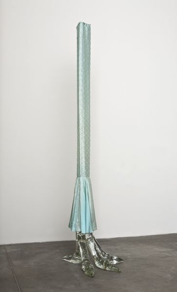 Zu sehen ist eine durchsichtige Glasskulptur aus Muranoglas in Form einer großen Vogelkralle mit einer hellblauen Seidenhusse, die wie ein (Hosen-)Bein anmutet.