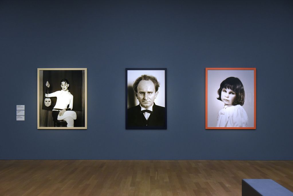 Drei Porträtfotografien in einem Ausstellungsraum auf blauer Wand. Gillian Wearing, Sammlung Goetz München