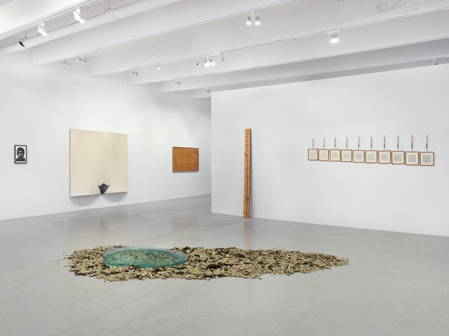 Exhibition room with a floor work made of brown leaves and a round, bluish glass plate on top, as well as two-dimensional works on the walls and an object leaning against the wall. Giuseppe Penone/Pino Pascali/Gilberto Zorio, Sammlung Goetz Munich 