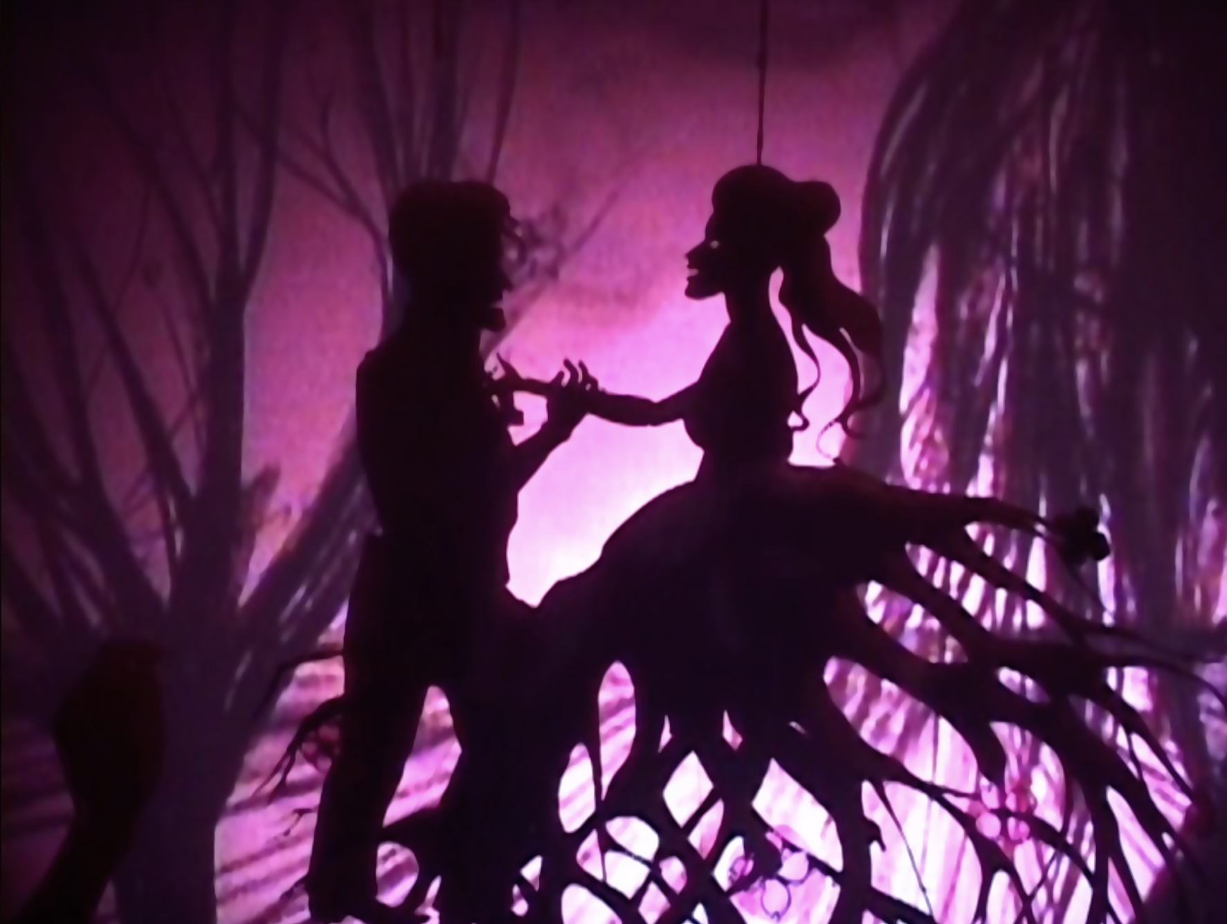 Silhouettes of a man and a woman (paper cut) stand out against a purple background. The skirt of the woman reminds of roots of a tree. 