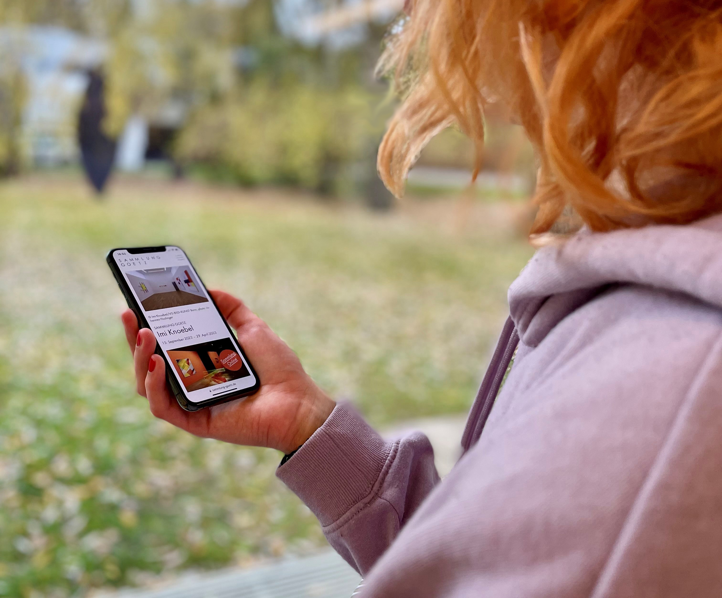 A hand holds a cell phone on which the website of the Sammlung Goetz is displayed