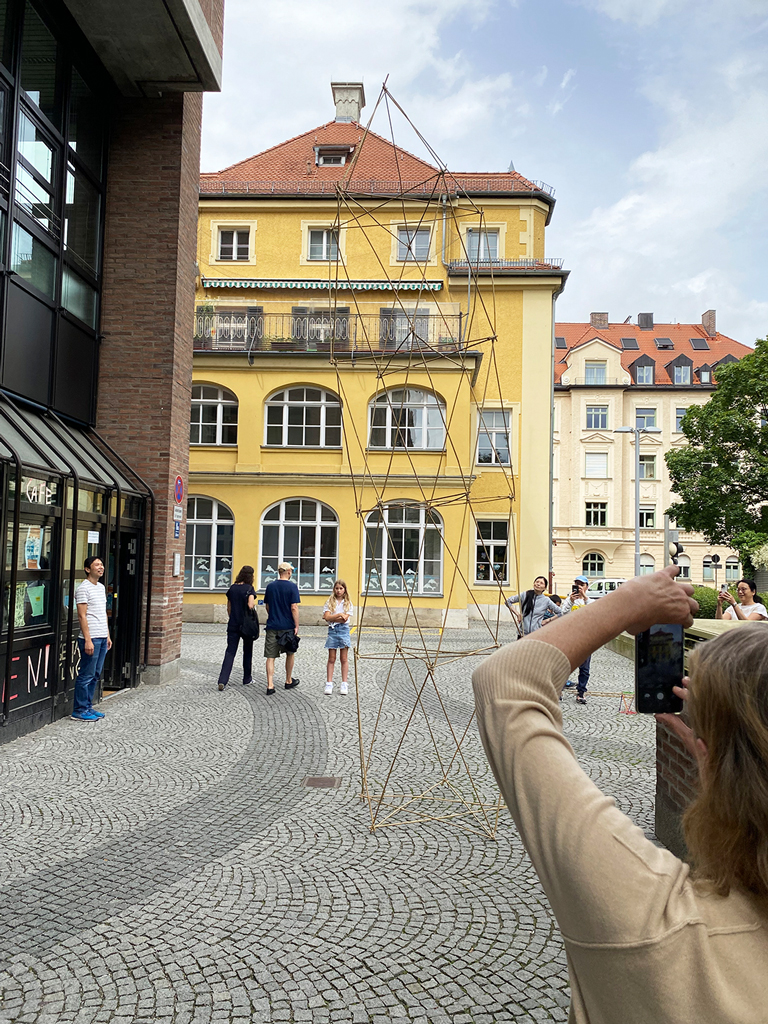 Eine räumliche Struktur aus dünnen Stäben steht in einem Innenhof