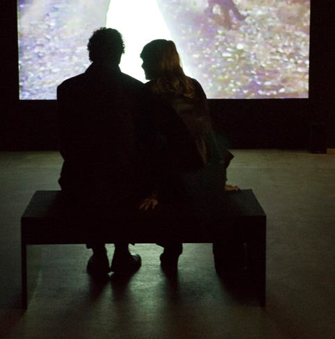 Zwei Menschen sitzen im Dunkeln vor einer Videoprojektion