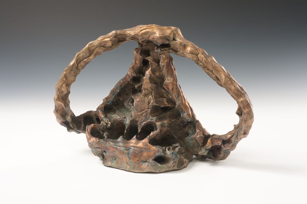 A bronze sculpture with a hand-shaped base and an arching element spanning over it.