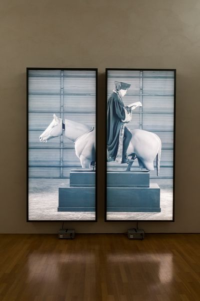 Lightbox dyptichon, shows a man in ancient clothing sitting backwards on a mechanical horse while reading a book. Rodney Graham, Sammlung Goetz, Munich. 