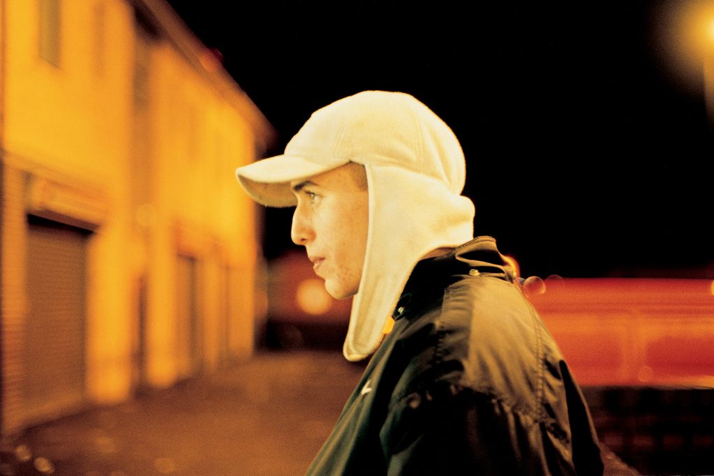 Photograph of a young man in profile at night, wearing a white, fluffy baseball cap with ear flaps. Tobias Zielony, Sammlung Goetz Munich