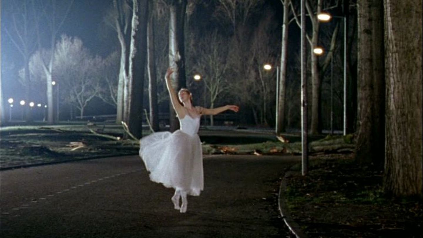 Video Still showing a ballet dancer dancing pointe in a white costume on a path in an illuminated park at night. Guido van der Werve, Sammlung Goetz Munich 
