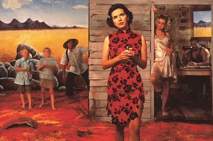 This photograph seems like a film still. A woman in a red dress stands thoughtfully in the foreground, holding glasses in her hands. Behind her, different stereotypes gather in front of a painted desert scenery.