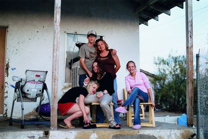 Fotografie einer unkonventionellen Familie in Freizeitkleidung auf einer Veranda eines heruntergekommenen Hauses. Tobias Zielony, Sammlung Goetz München