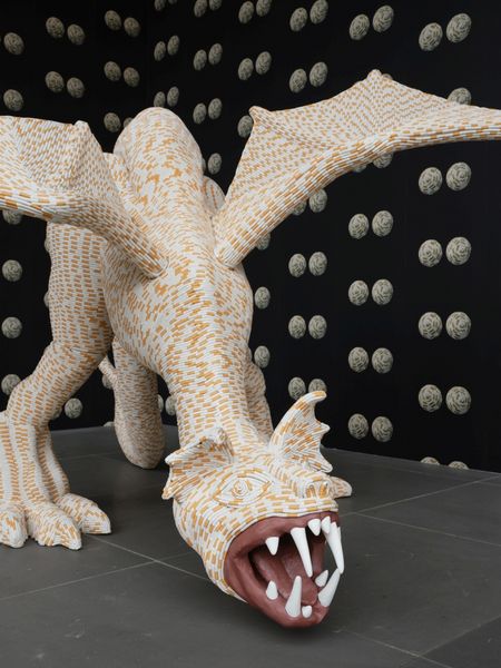 Sculpture of a dragon, covered with cigarettes. On the wall behind it a wallpaper with pairs of balls, also covered with cigarettes