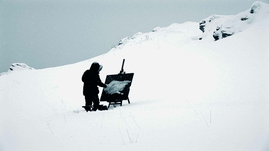 Dieser Video Still zeigt eine Person, die auf einem verschneiten Berg vor einer Staffelei mit schwarz grundierter Leinwand steht und darauf eine weiße Fläche malt. Barnaby Hosking, Sammlung Goetz München