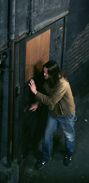 Die Fotografie des Künstlers Jeff Wall zeigt einen langhaarigen und bärtigen Mann, der gerade dabei ist, eine Tür in einer düsteren Gasse zu öffnen. Dabei wirkt er lauschend und vor allem vorsichtig. Das Foto scheint aus der Perspektive einer oberen, gegenüberliegenden Wohnung gemacht worden zu sein.