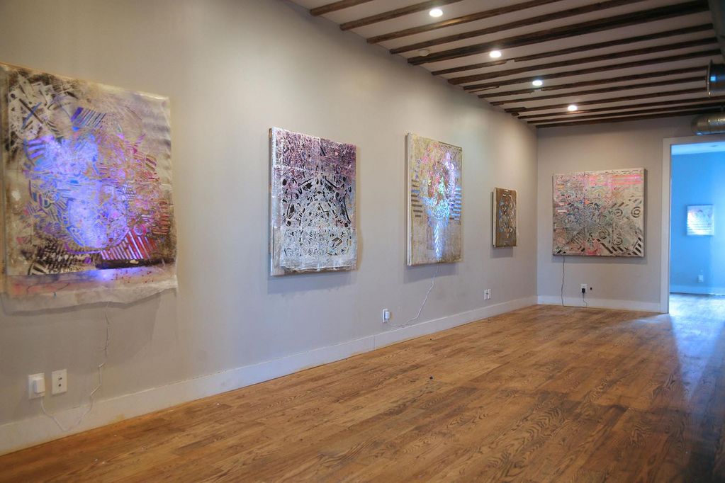 Exhibition space with paintings by Lane Twitchell. Some canvases are backlit with colored LED lights, others are painted with shimmering colors.