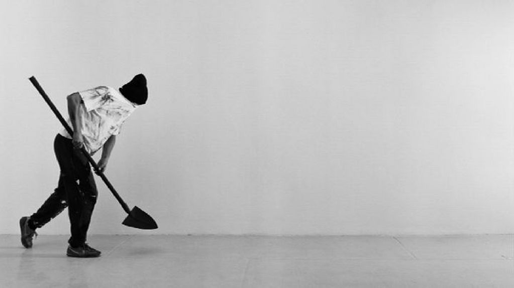 Die Schwarz-Weiß-Aufnahme zeigt eine vermummte Person mit einer Schaufel in den Händen. Robin Rhode, Sammlung Goetz München