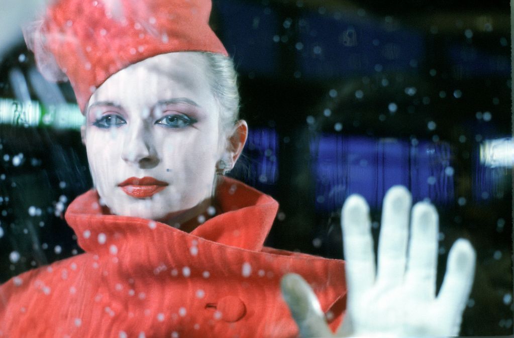 Production Still, Frau in Roter Stewardess-Uniform und rot geschminkten Lippen hält eine Hand an eine verregnete Glasscheibe. Ulrike Ottinger, Sammlung Goetz, München