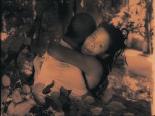 Image in sepia tones. A woman embraces a man. Plants frame the scene