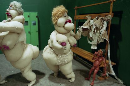Das Video Still zeigt zwei sehr dicke, nackte und weiße Frauenpuppen aus Stoff in einer Umkleide zusammen mit einem kleinem schwarzen Jungen aus Plastilin. Nathalie Djurberg & Hans Berg, Sammlung Goetz München