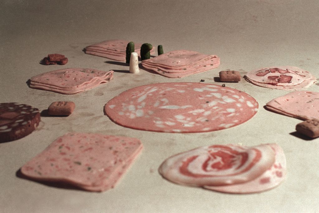 Simple representation of a carpet shop consisting of different kinds of sausage cuts and figures made of pickles.